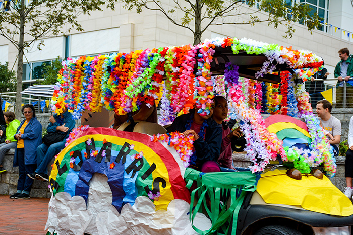 A golf cart decorated with rainbows, rides through the Homecoming parade